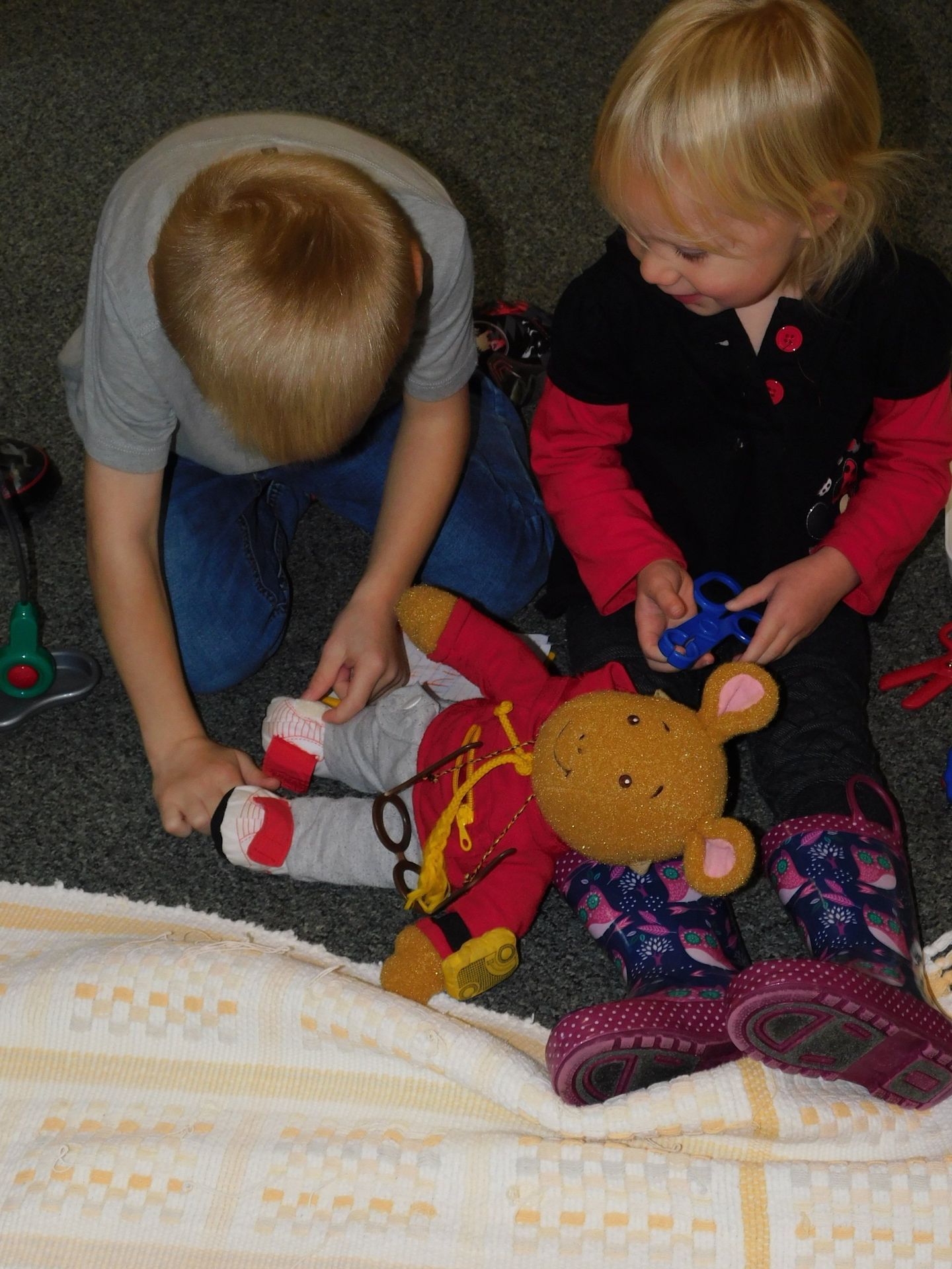 Two children tending to a teddy bear on a blanket