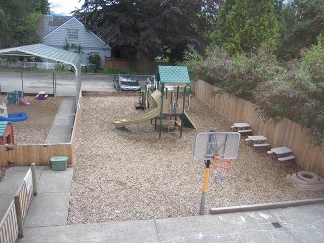 Playground with wood chip ground, play structure, basketball hoop, and wooden fence