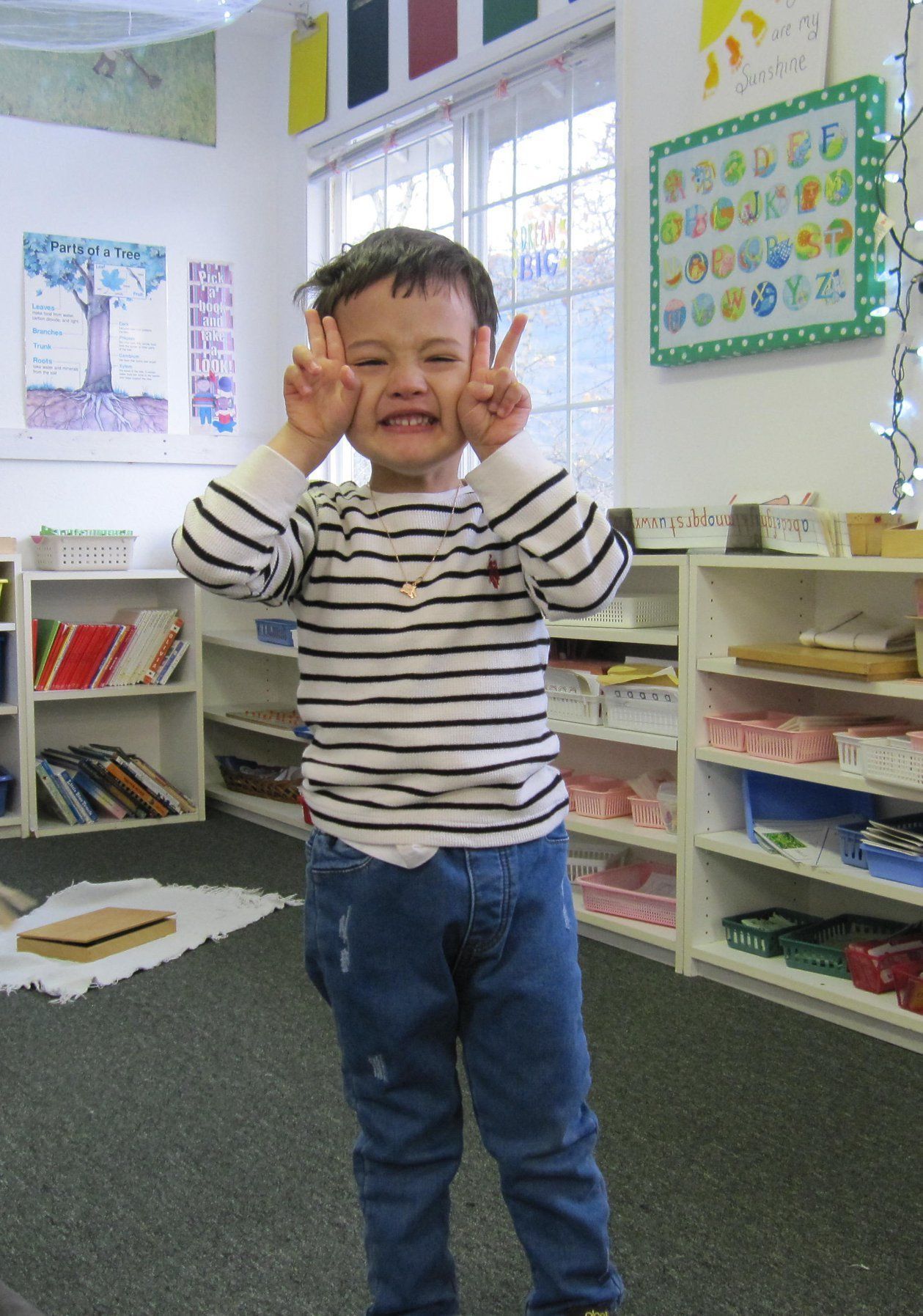 Boy in striped shirt and jeans makes peace signs in a classroom