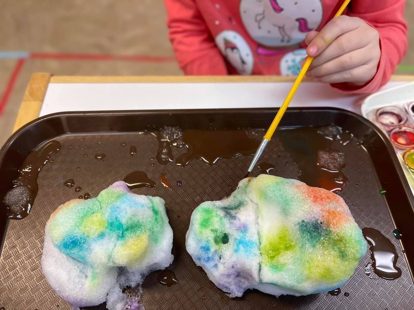 Child paints colorful foam on a tray with a paintbrush