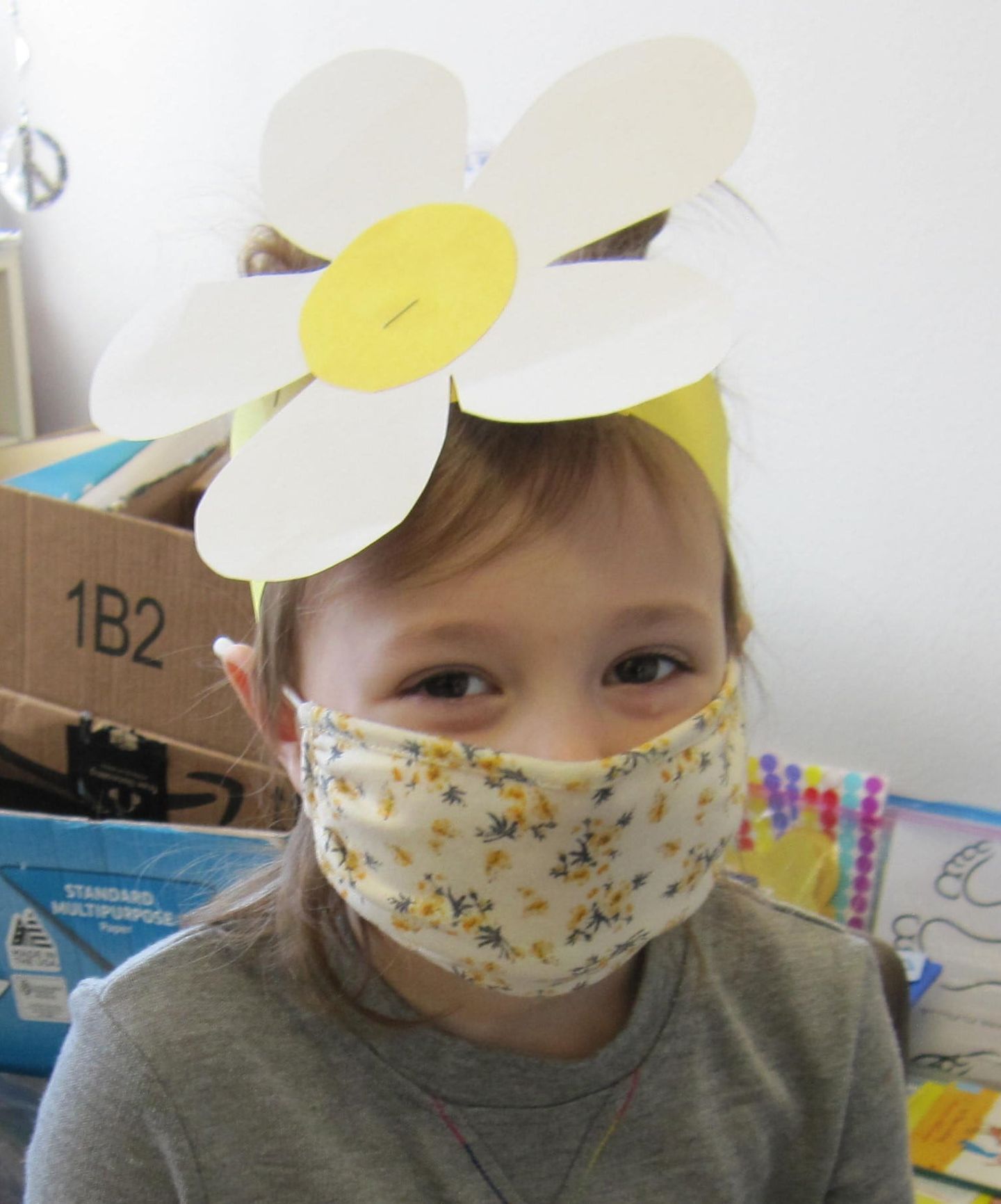Girl wearing a daisy crown and floral face mask smiles at the camera