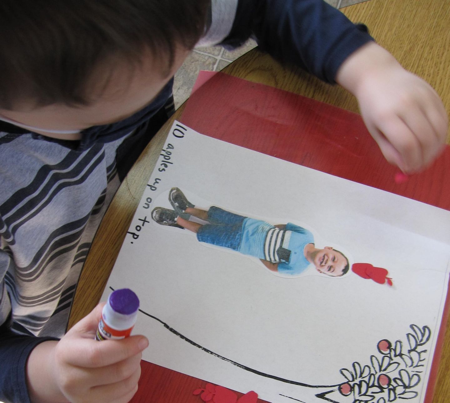 Child gluing red pieces on a drawing of a boy lying down