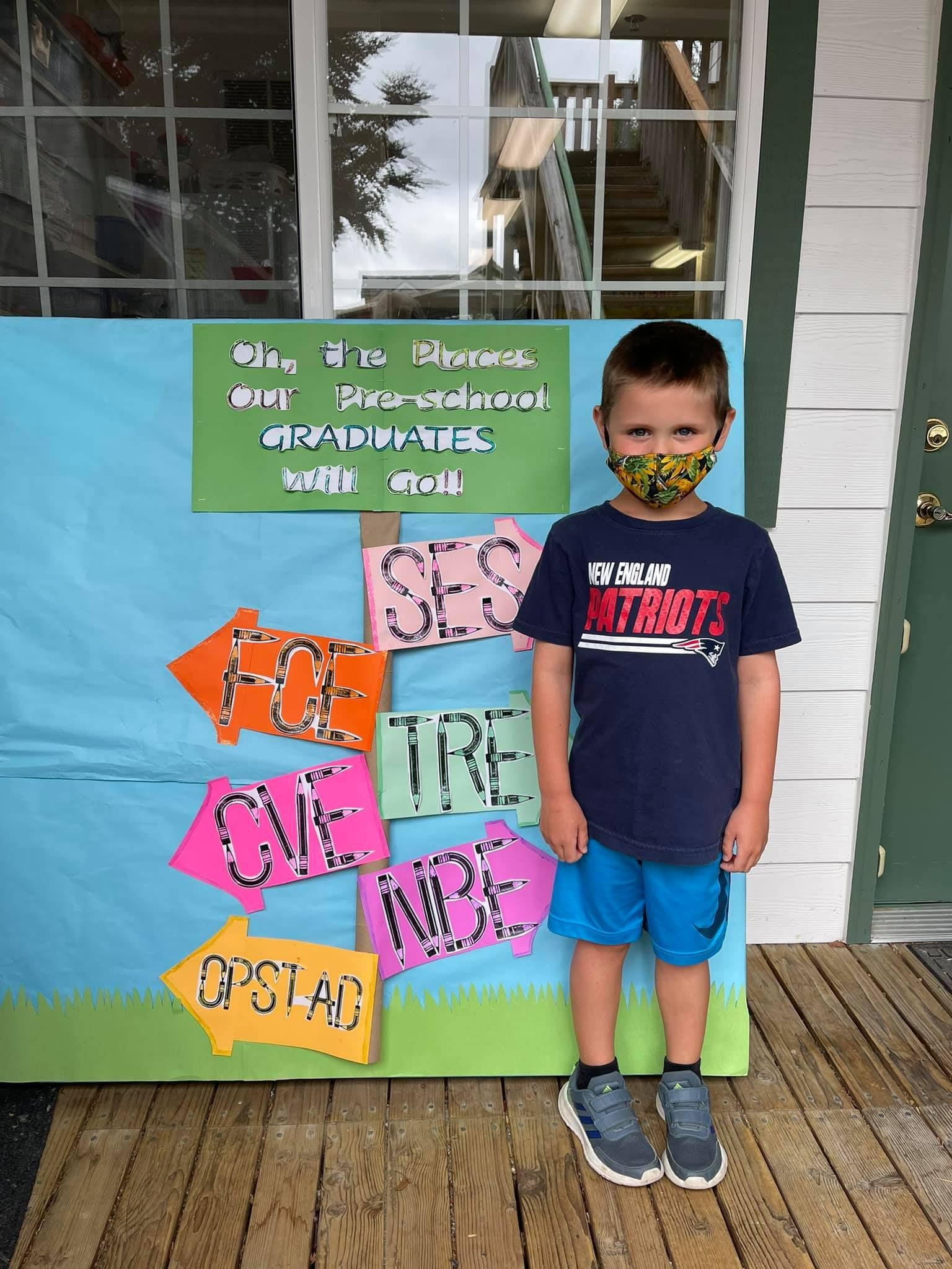 Boy in mask stands near a sign with words, colorful arrows, and a green background