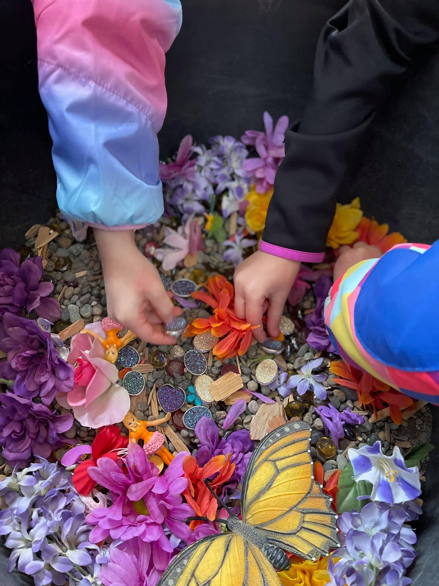 Children's hands playing in a bin filled with colorful flowers