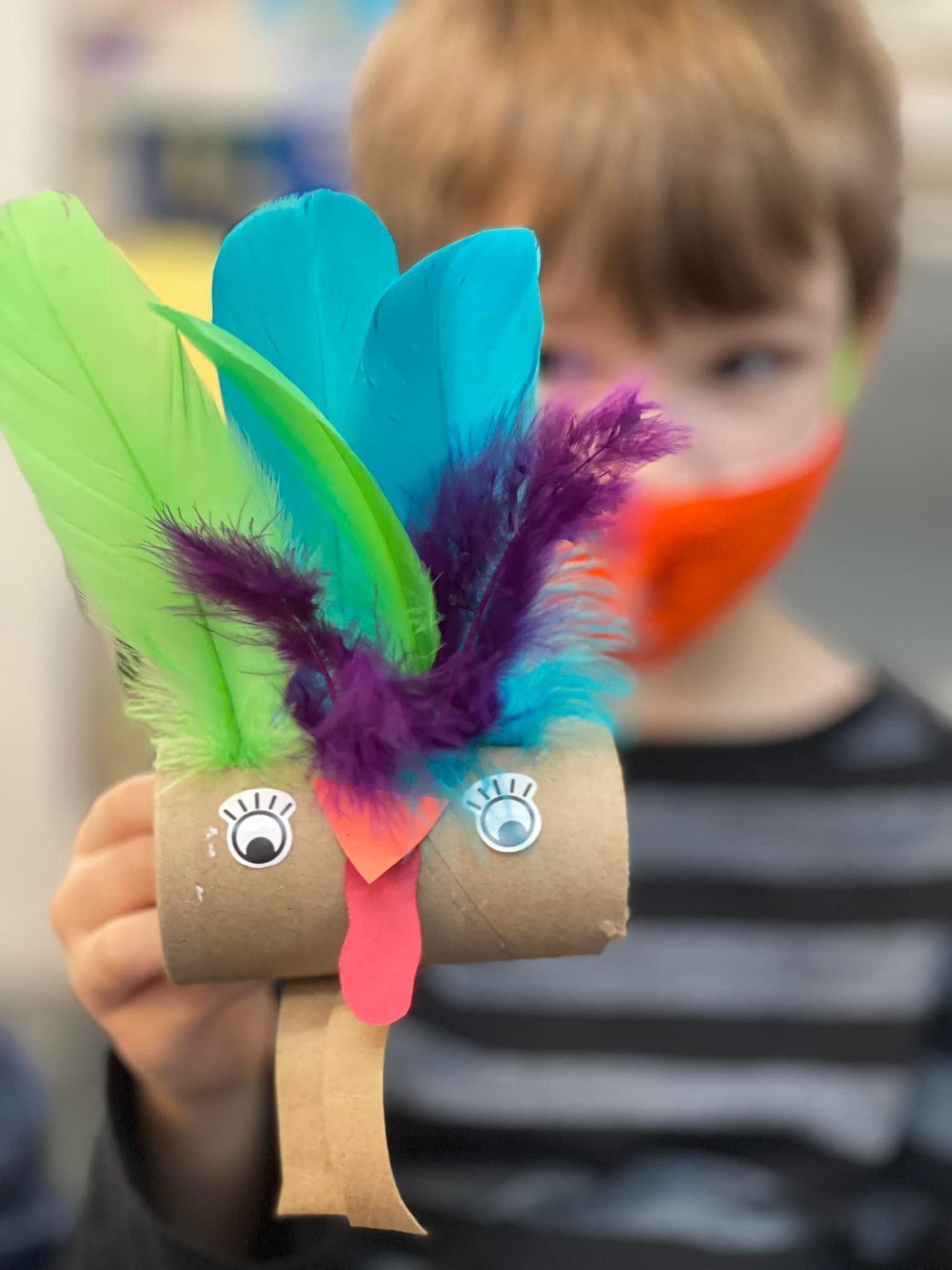 Boy holding a craft bird made from a toilet paper tube with feathers