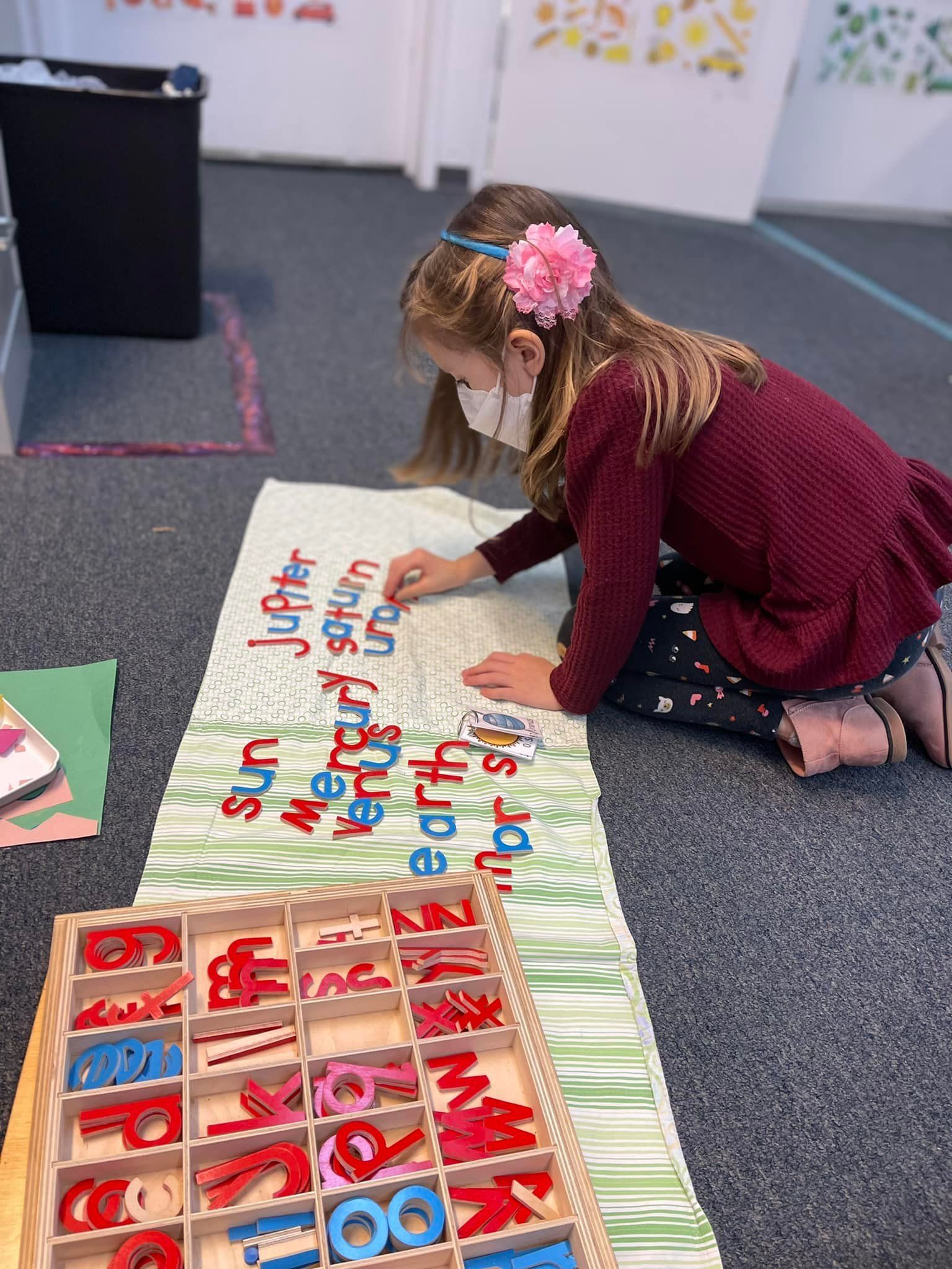 Girl wearing a mask arranges wooden letters on a mat
