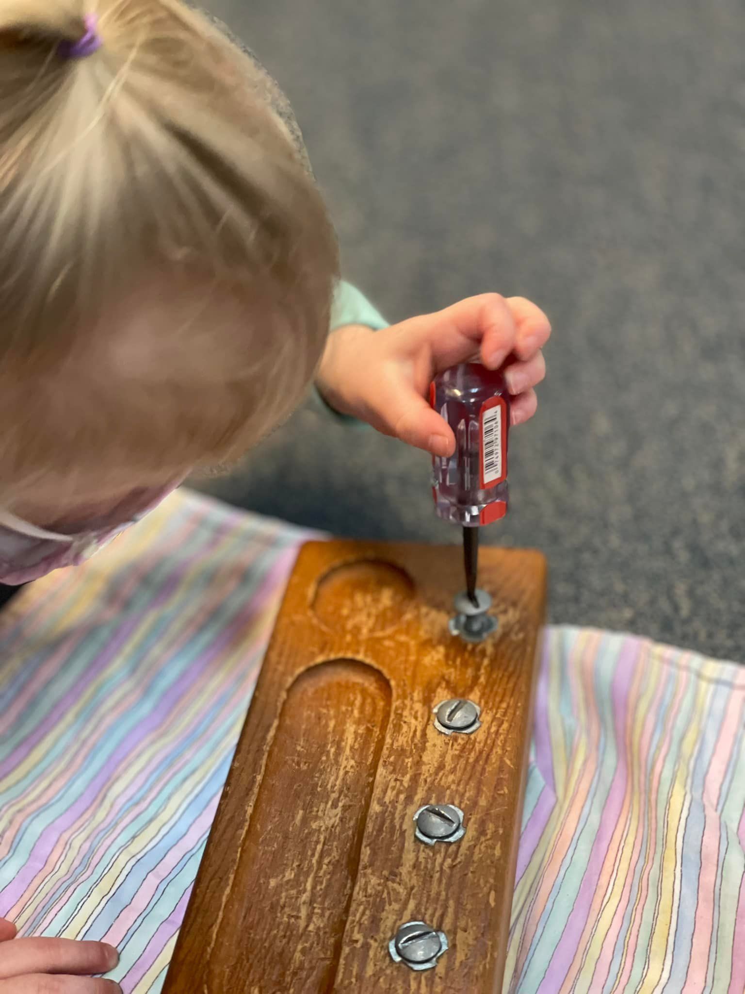 Child using a screwdriver on a wooden board with screws