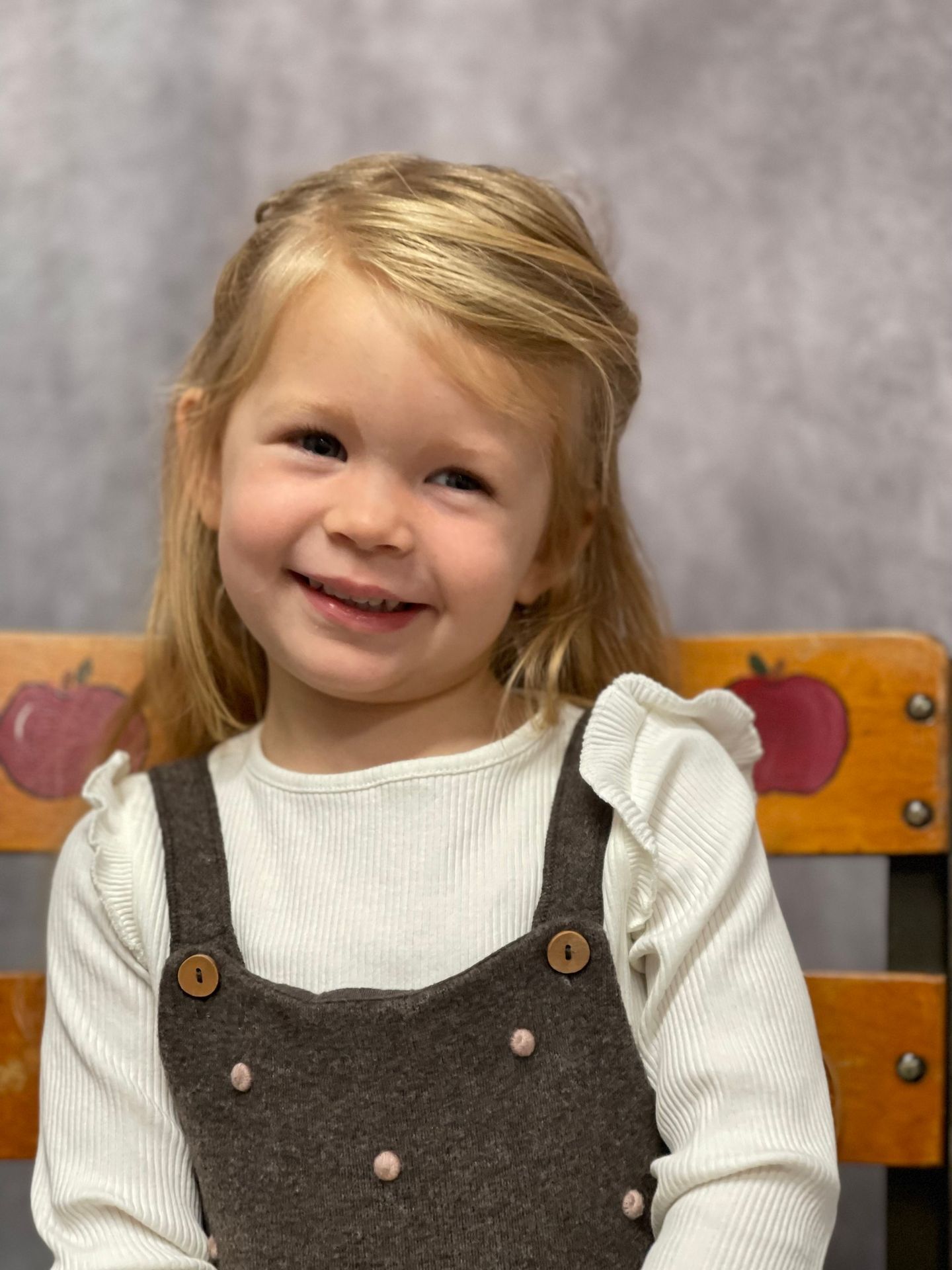 Smiling young girl with blonde hair in a brown overall and white shirt; sitting