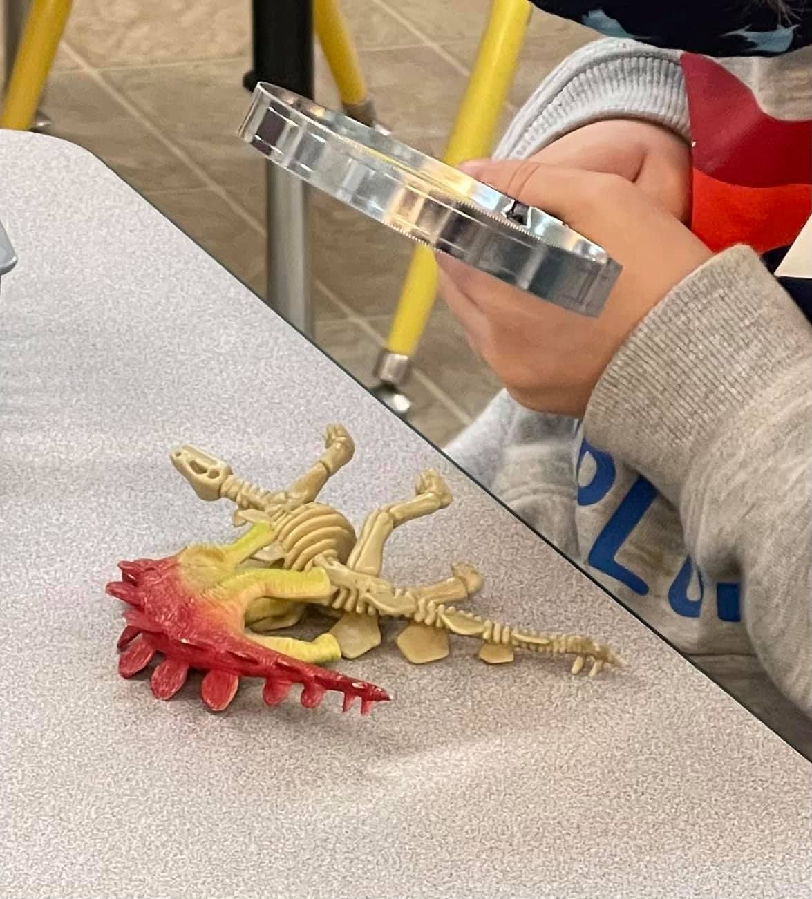 Child examining dinosaur toy with magnifying glass at a table
