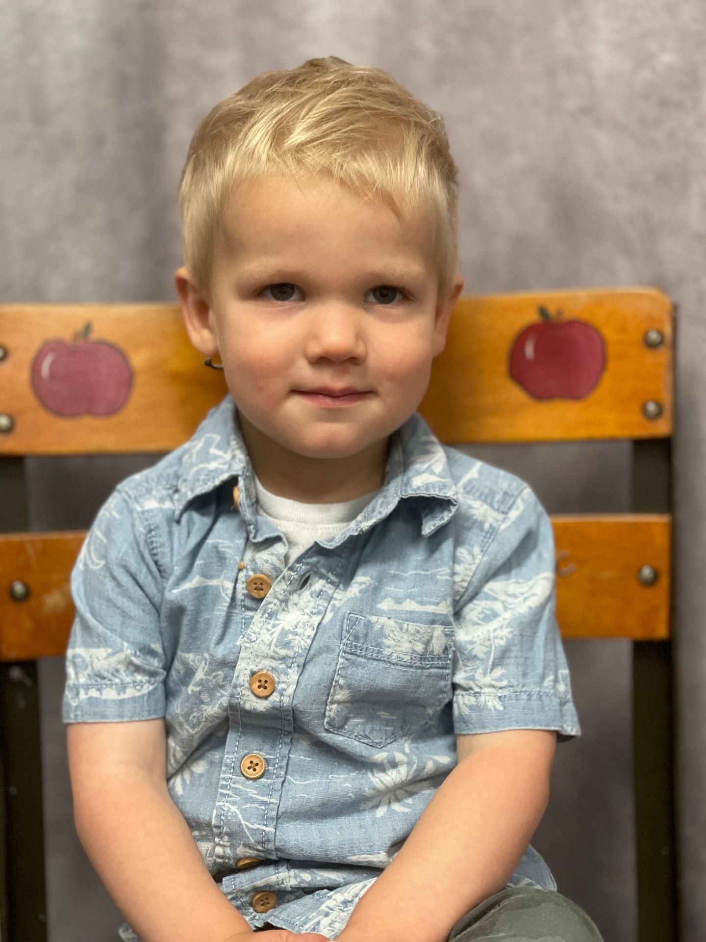 Blond toddler in blue shirt, seated on a chair with apple decorations