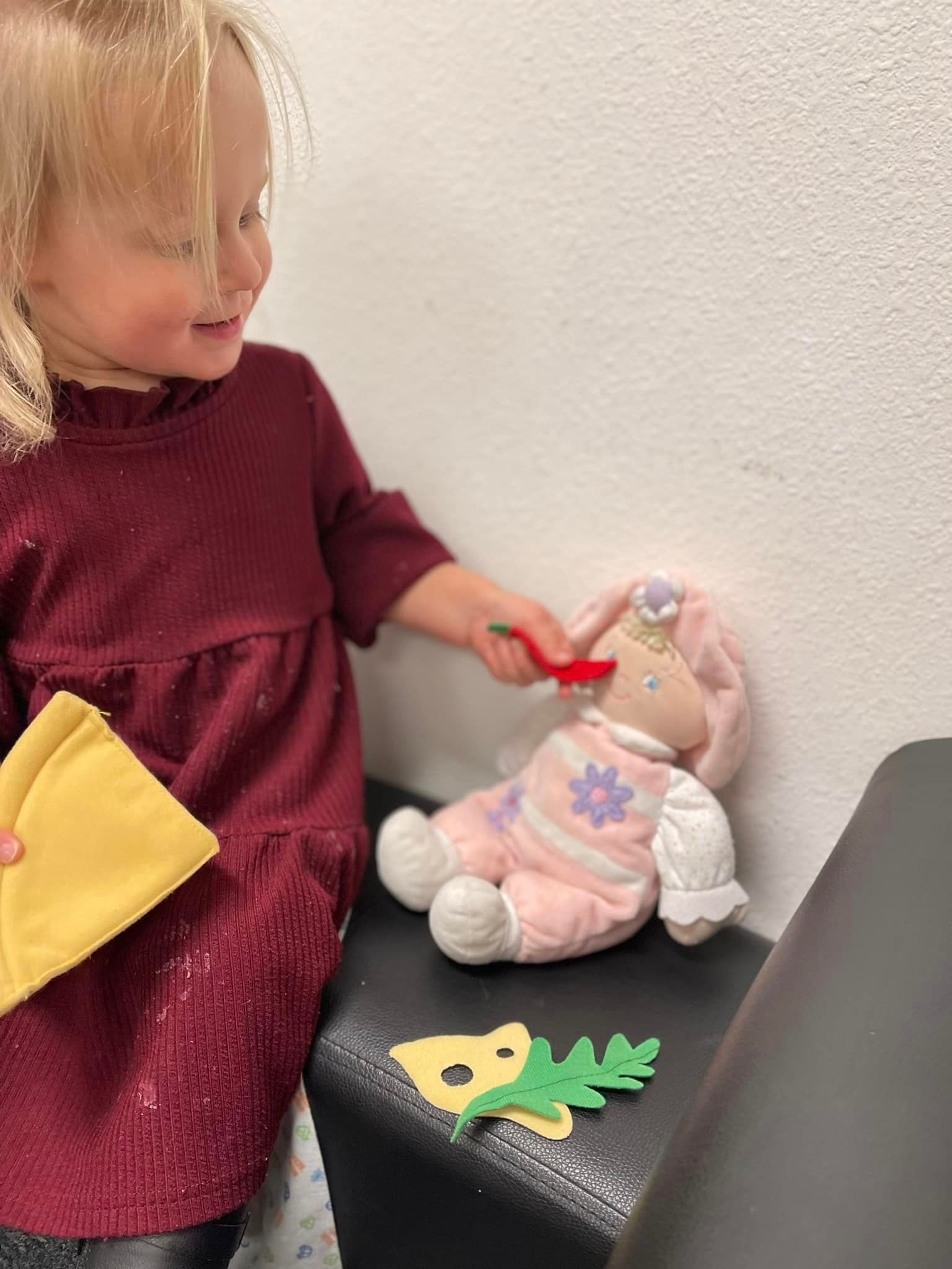A young girl feeds a bunny doll, smiling, indoors