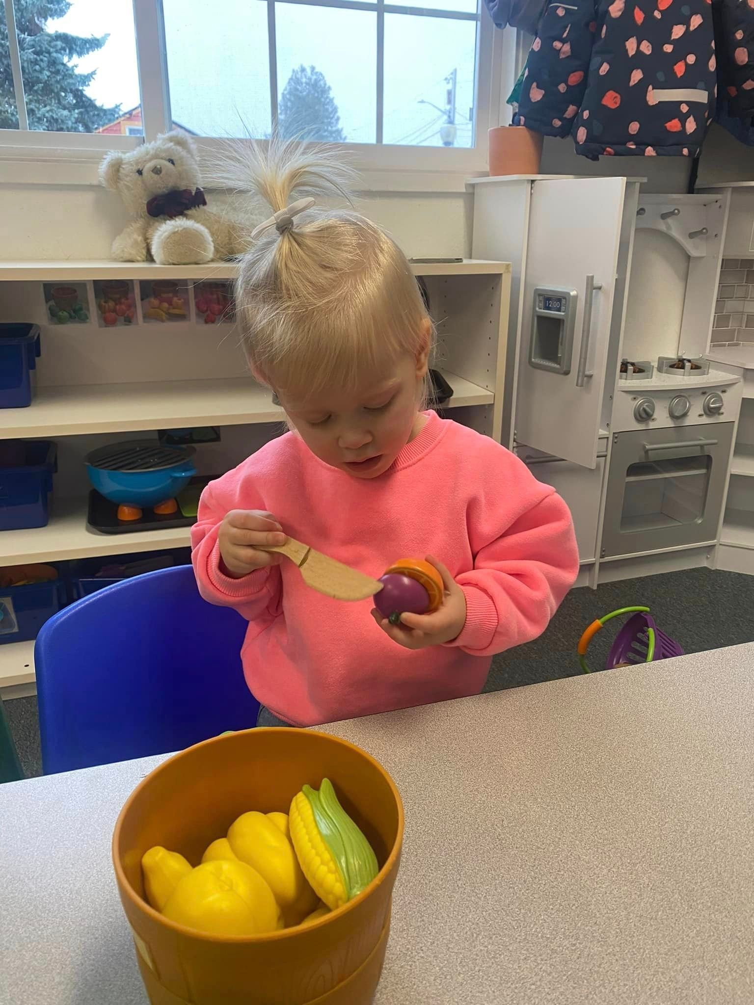 Young child in pink sweater playing with toy food in a classroom setting