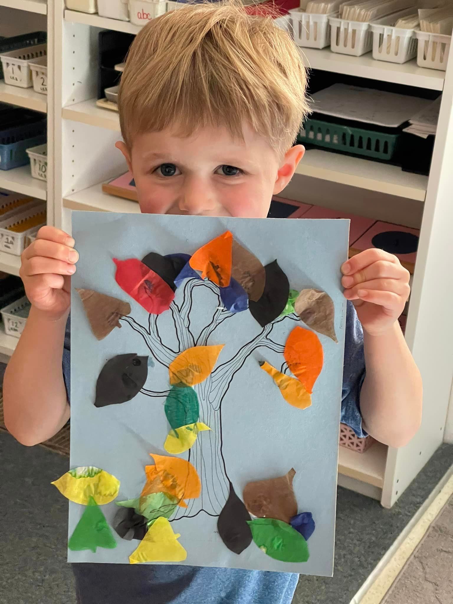 Boy holding a tree art project with colorful paper leaves
