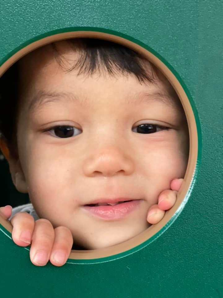 Young child peeking through a green circular opening, smiling