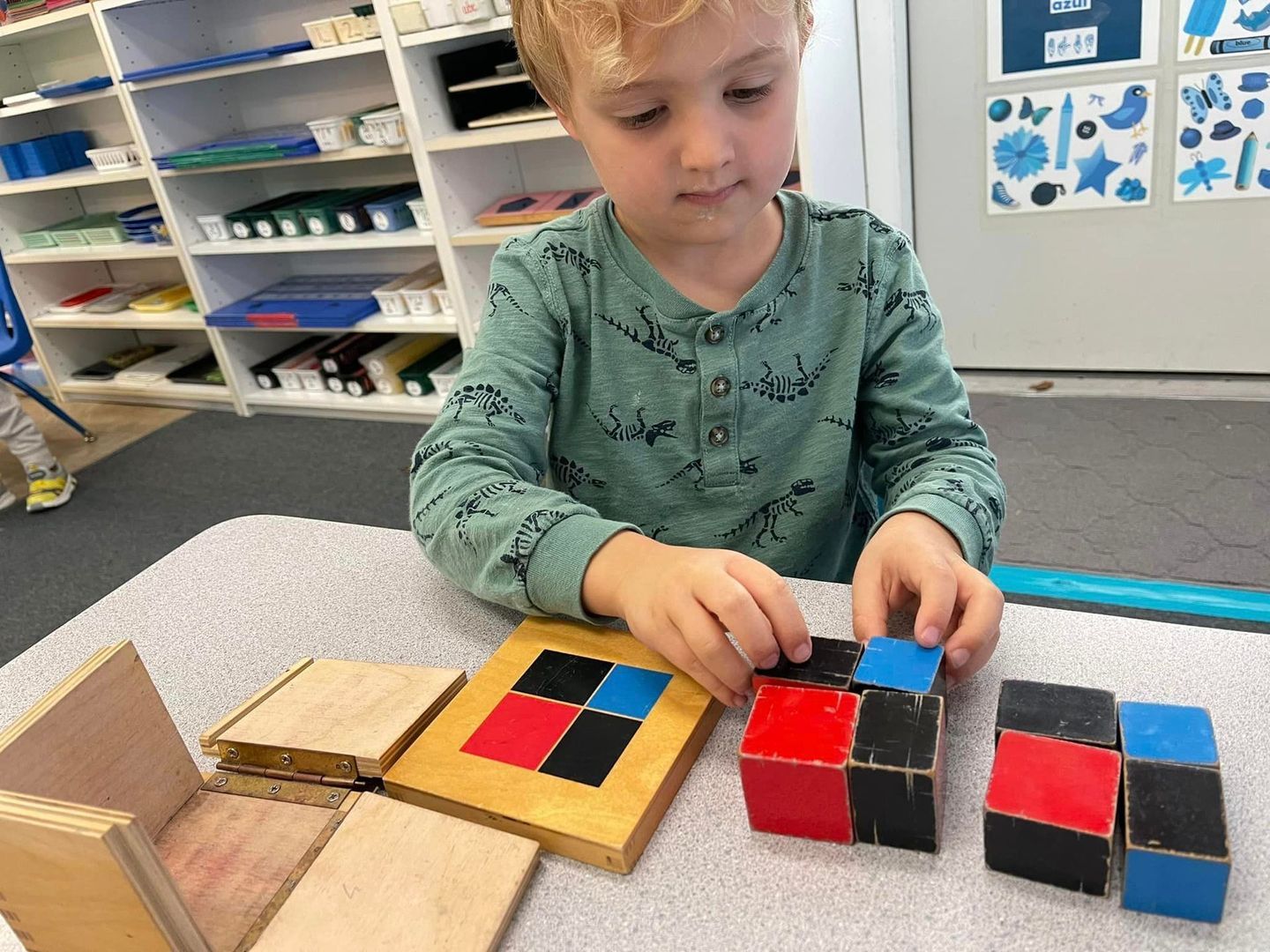 Young boy assembling colorful wooden blocks at a table in a classroom