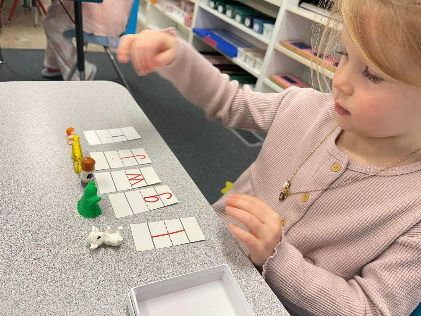 Young child arranging toy animals with word cards on a table