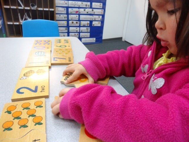 Young girl in pink jacket arranging number cards on a table