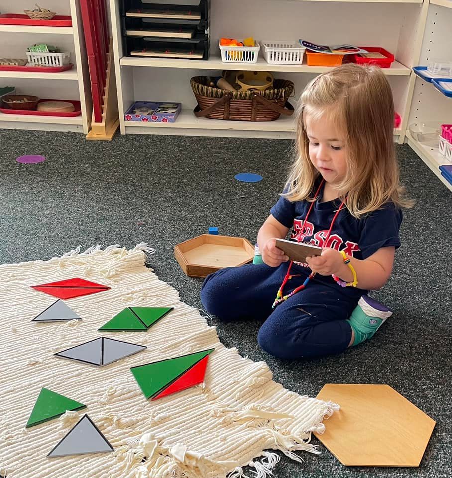 Young girl playing with geometric shapes on a rug in a classroom setting