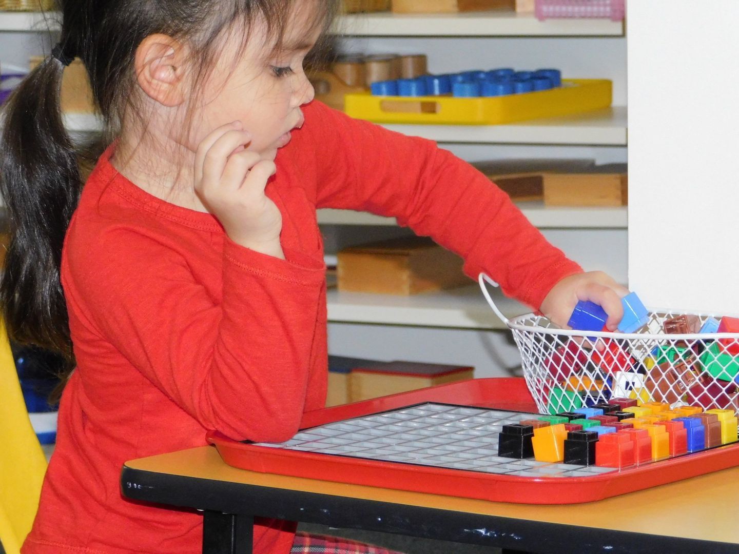 Girl in red shirt playing with colorful blocks at a table in a classroom