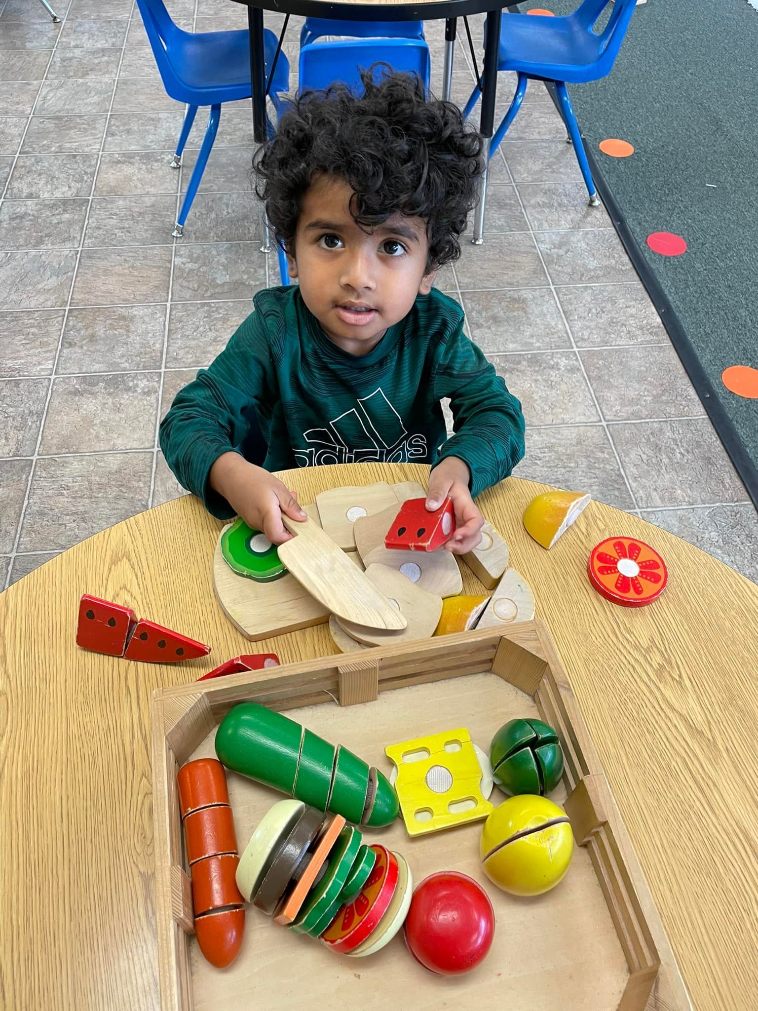 Boy playing with wooden toy food at a table, looking at the camera