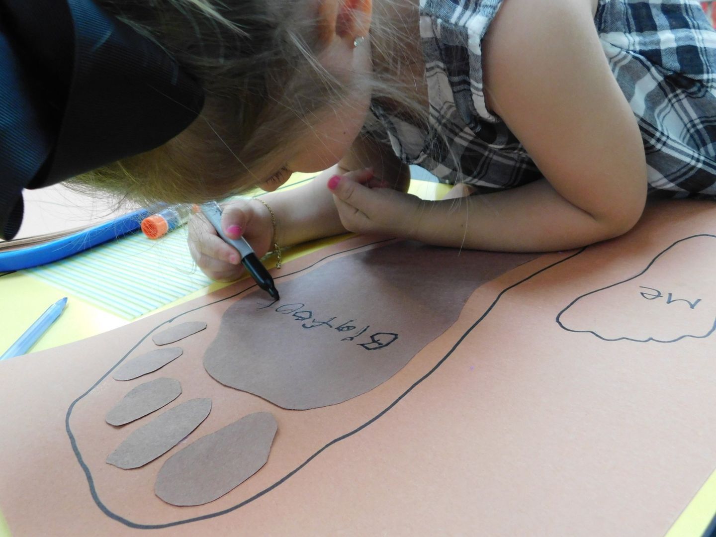 Young child writing on a brown bear paw outline with a black marker on paper