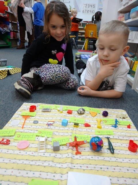 Two children looking at a display of objects on a mat in a classroom