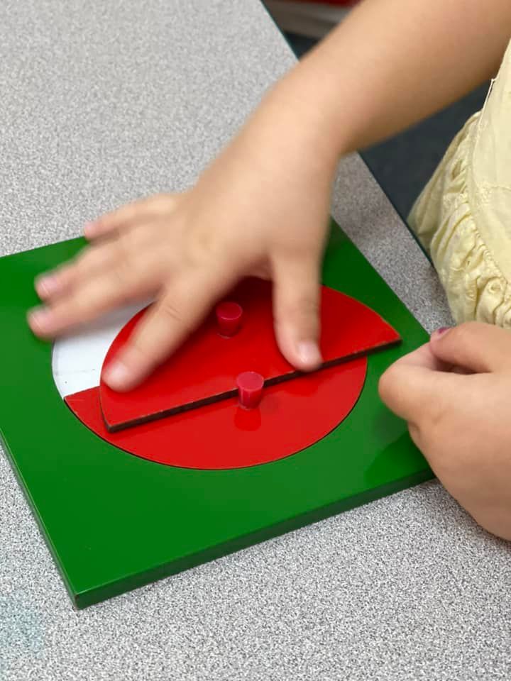 A child's hand manipulates a red and green fraction learning tool on a table