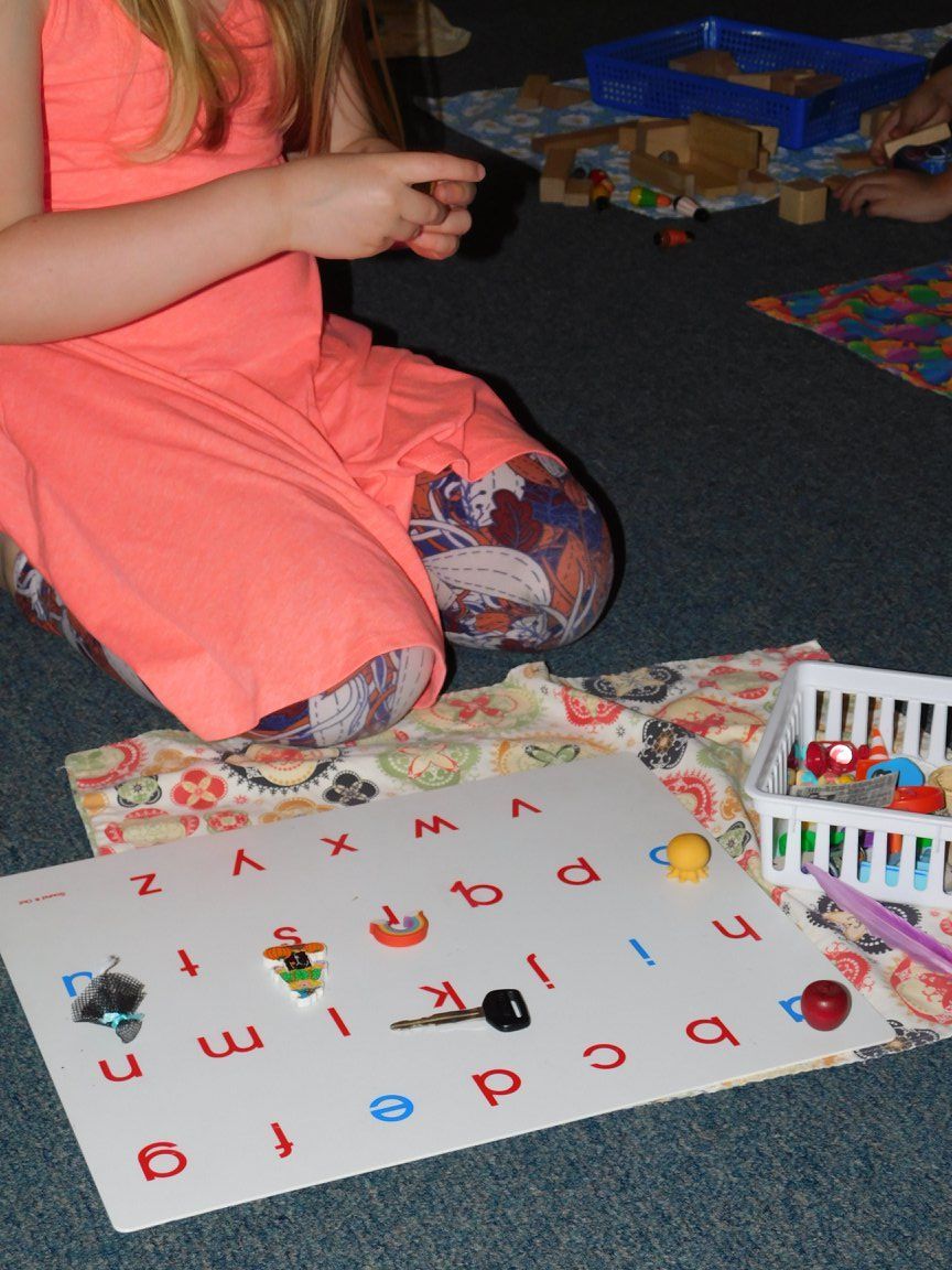 Girl playing with letters and objects on a whiteboard, sitting on a floor