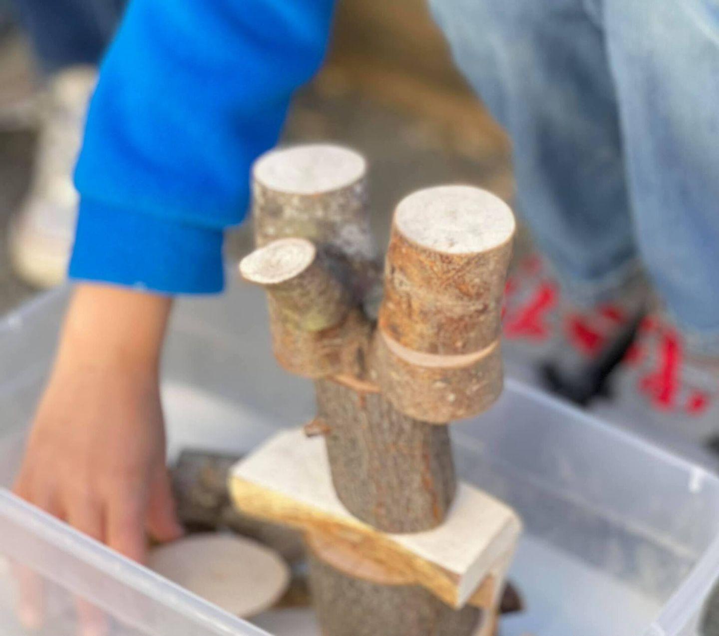 Child stacking wooden blocks and tree branches in a plastic container