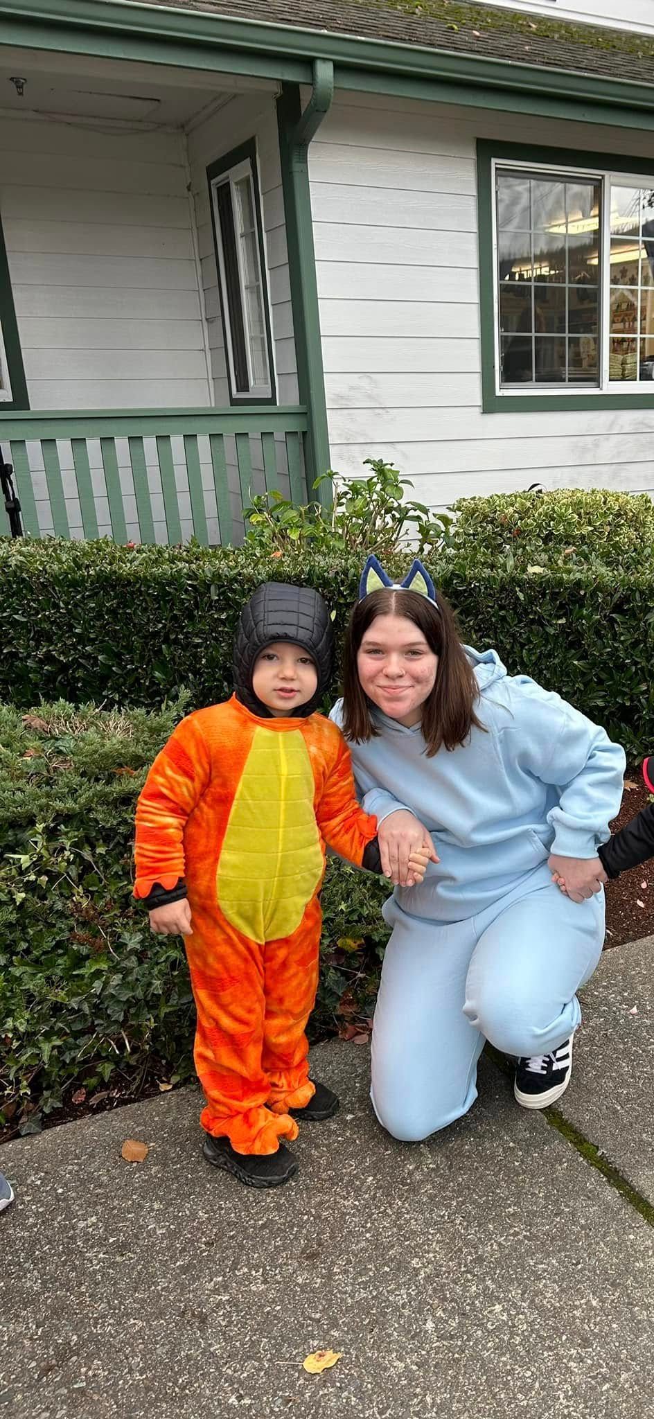 A child in an orange costume and an older person holding hands in front of a house
