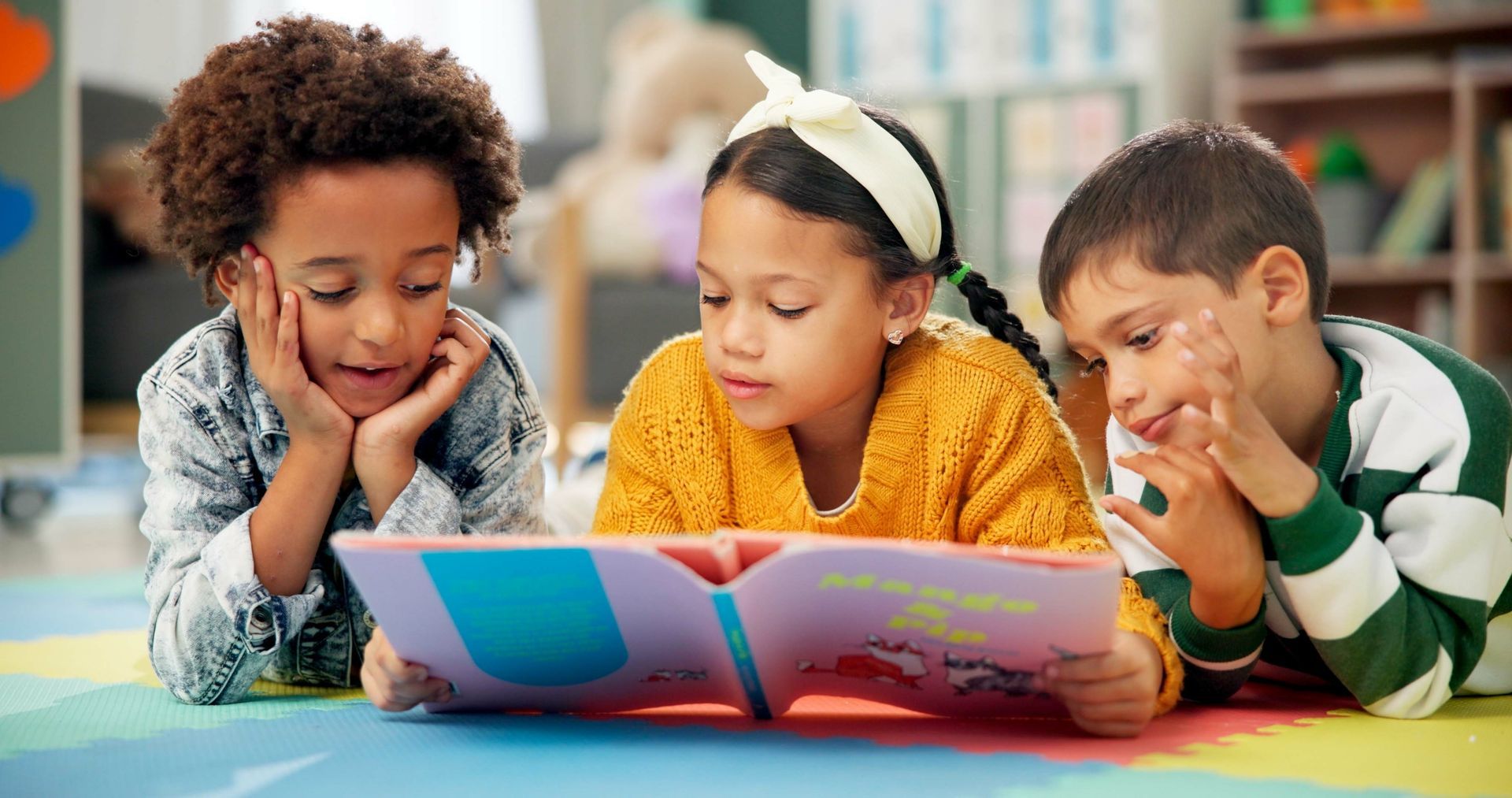 Three children reading a book together on a colorful mat