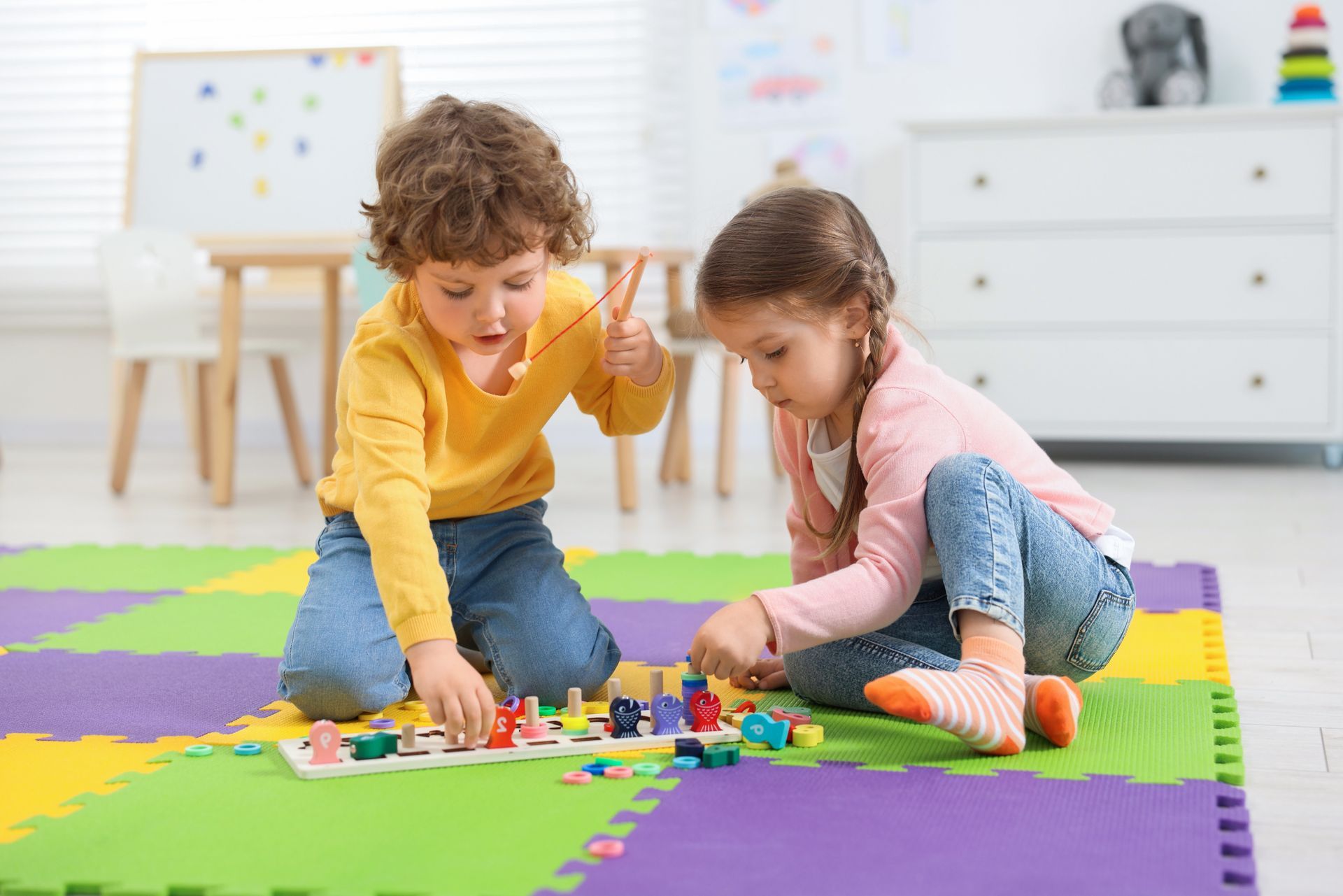 Two children playing a board game on a colorful mat in a playroom