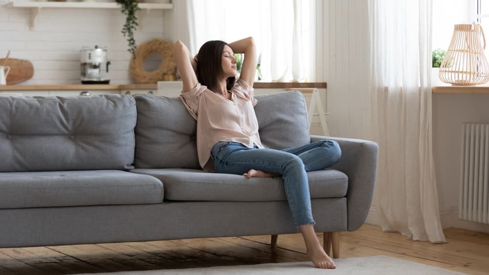 A Woman Is Sitting on A Couch in A Living Room with Her Arms Outstretched - Healthy Cleaning Solutions in Scotts Head, NSW