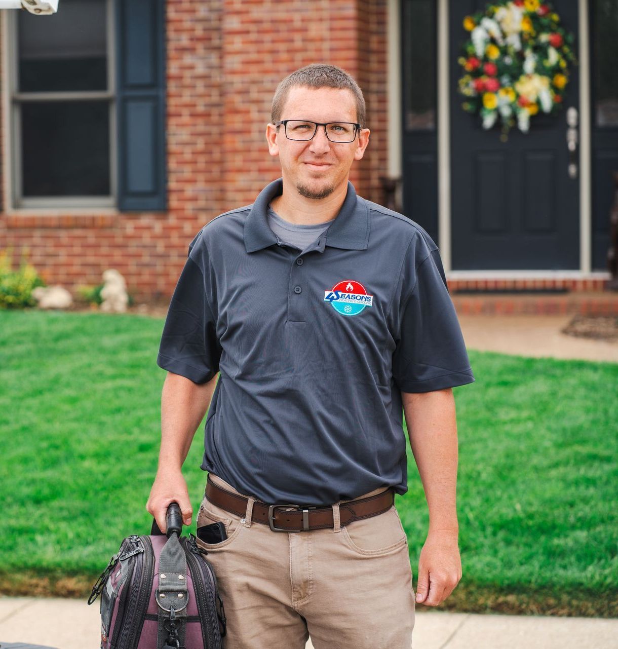 A man is standing in front of a brick house holding a backpack.