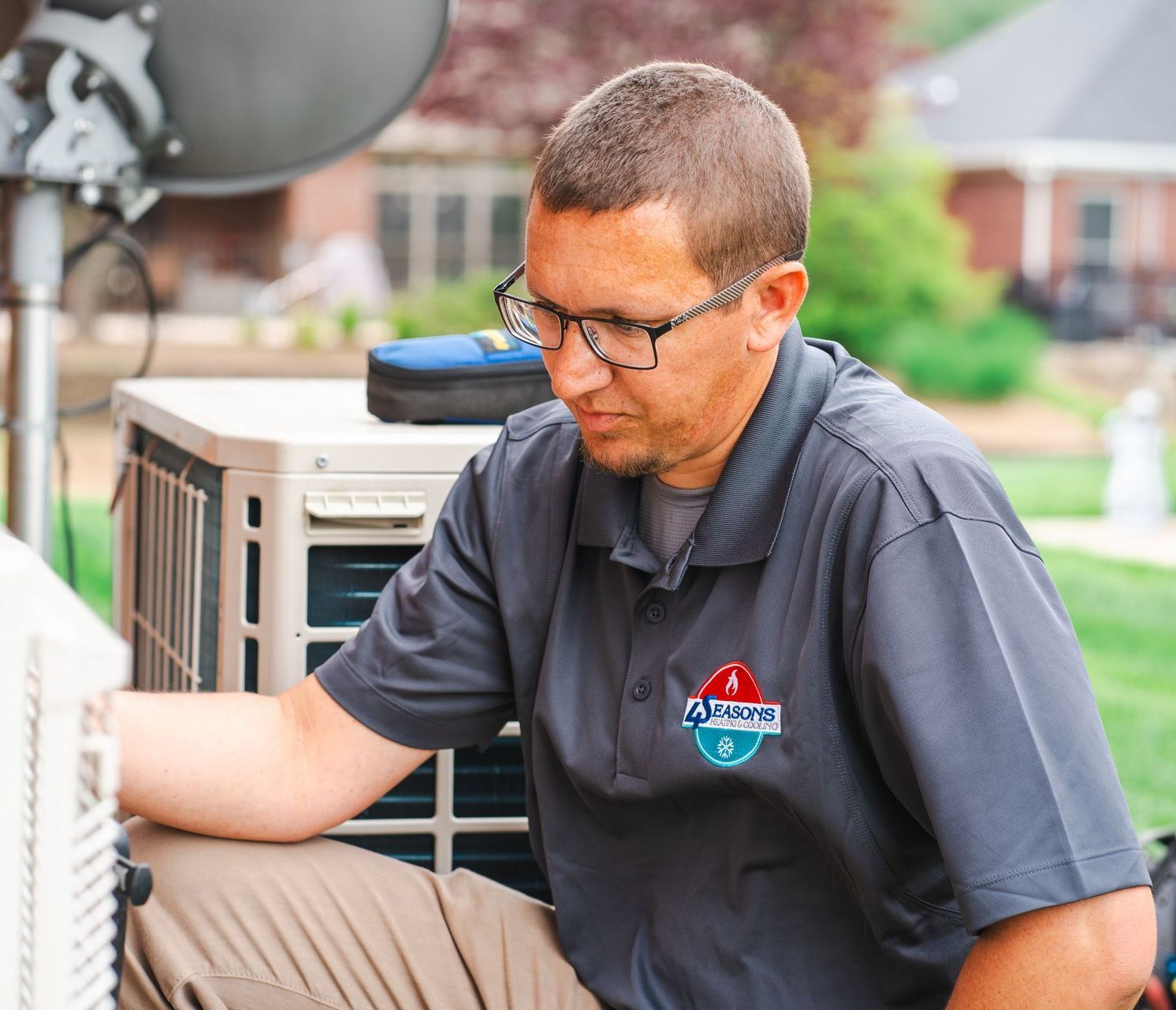 A man wearing glasses is working on an air conditioner outside.