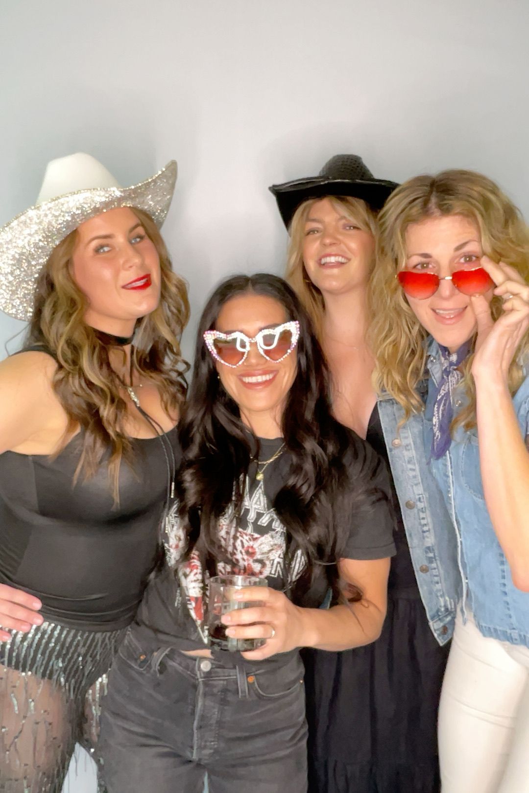 Four people posing for a photo.  They wear sunglasses, hats, and a mix of casual/party attire; expressions are playful.