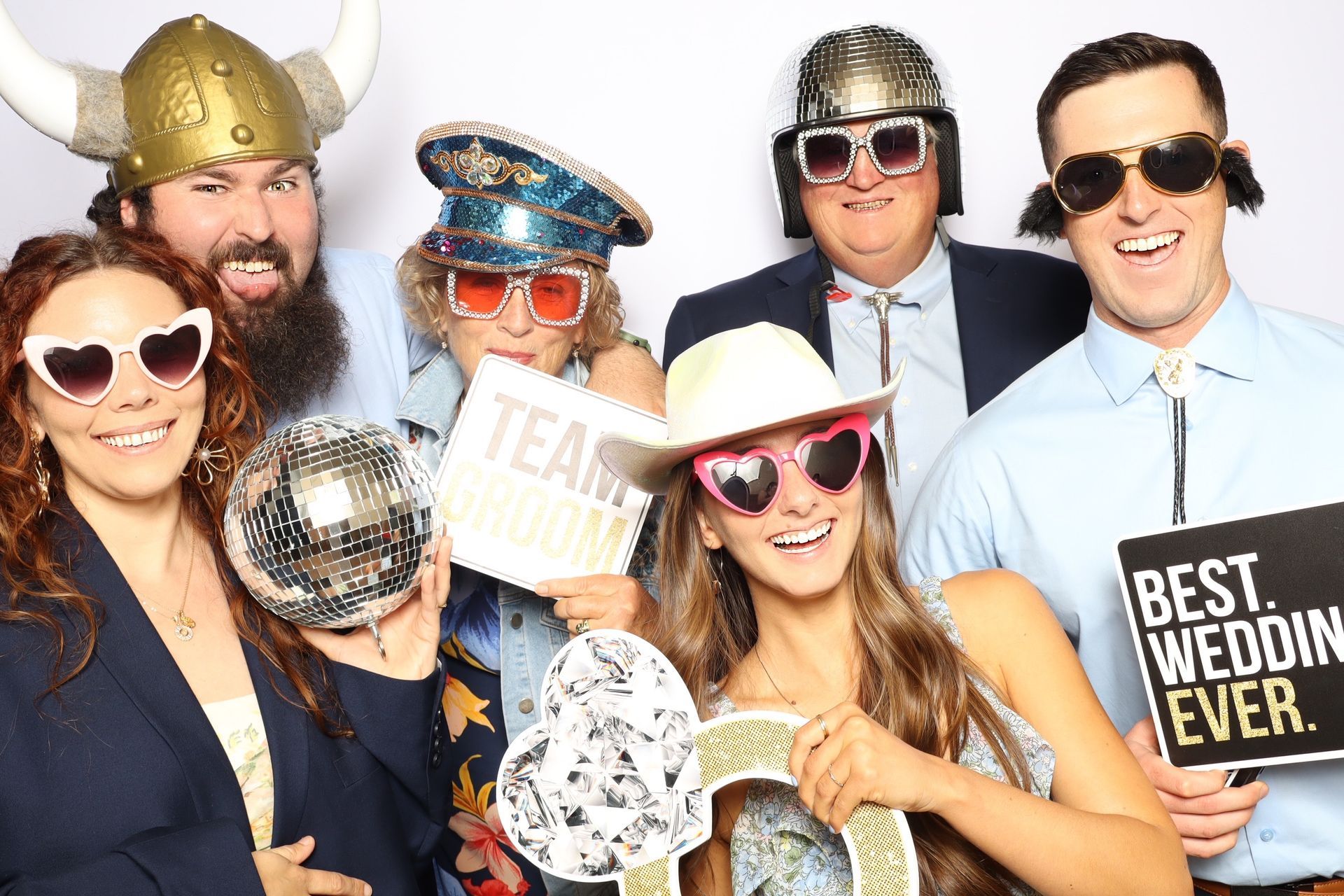 Group photo booth fun: people in silly hats and sunglasses holding props.