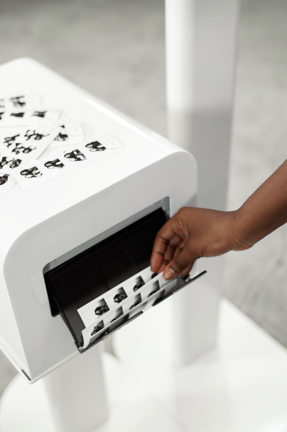 Hand reaching into a white kiosk to pull out a sheet of printed items, in a light setting.