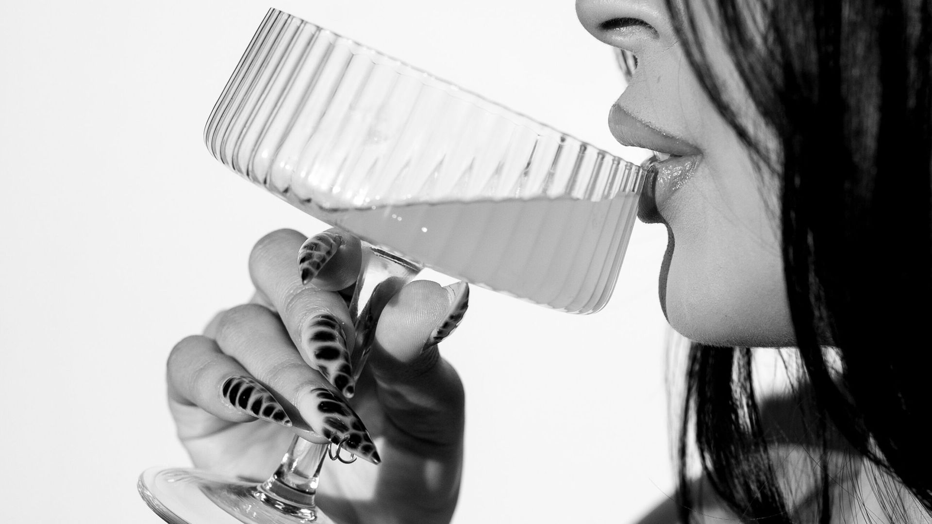 Woman drinking from a tall, angled glass. Long, patterned nails are visible.