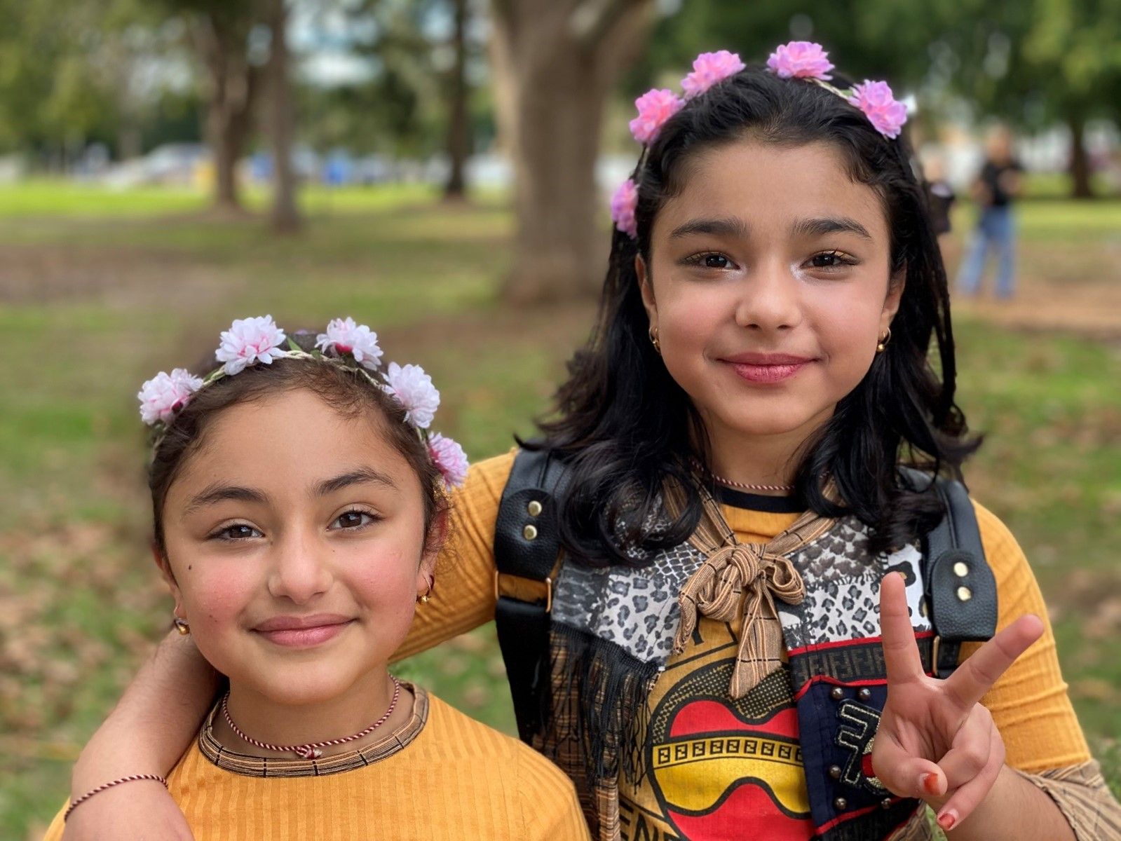 Two young girls wearing flower crowns are posing for a picture in a park.