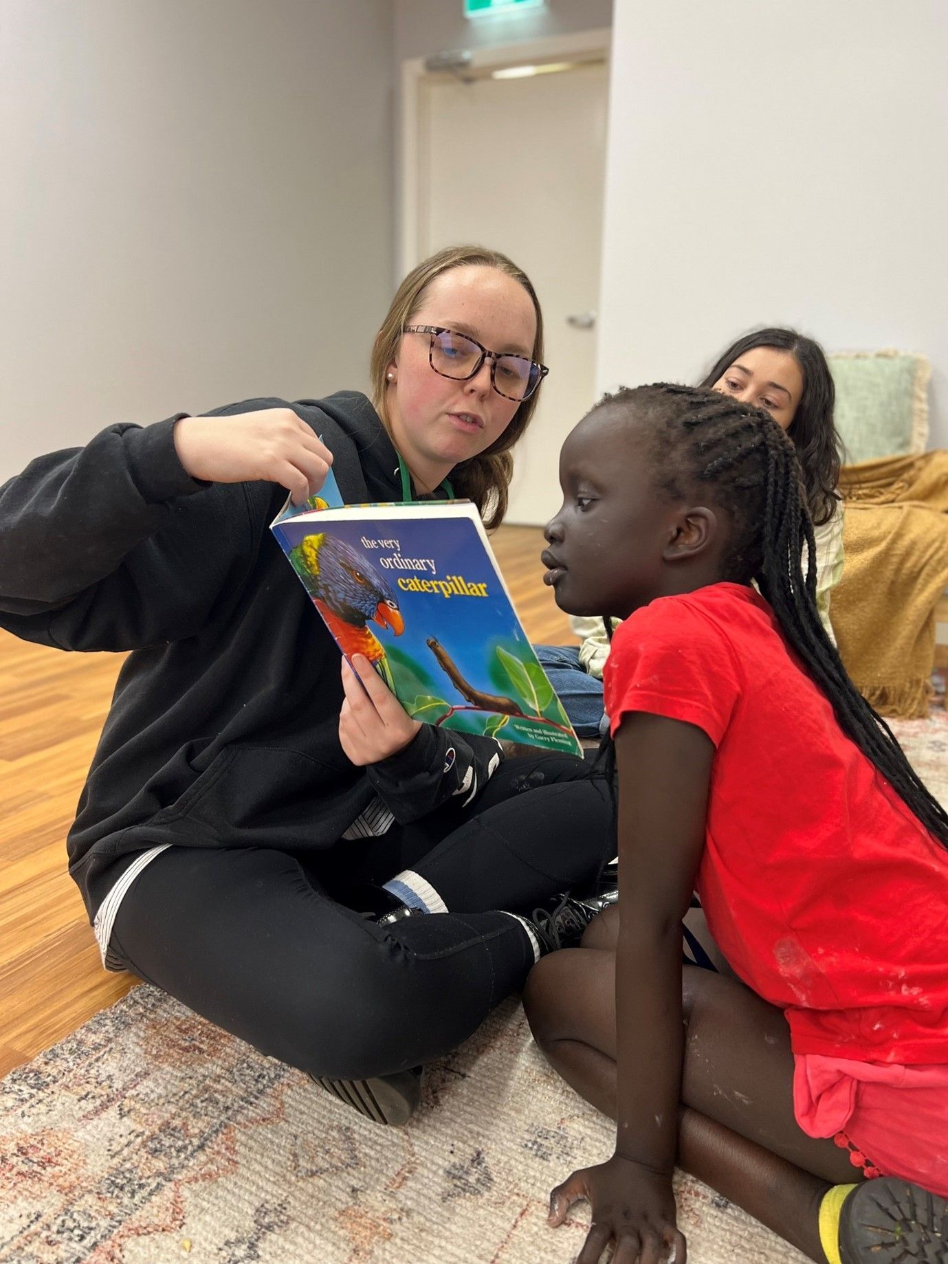 A woman is sitting on the floor reading a book to a young girl.