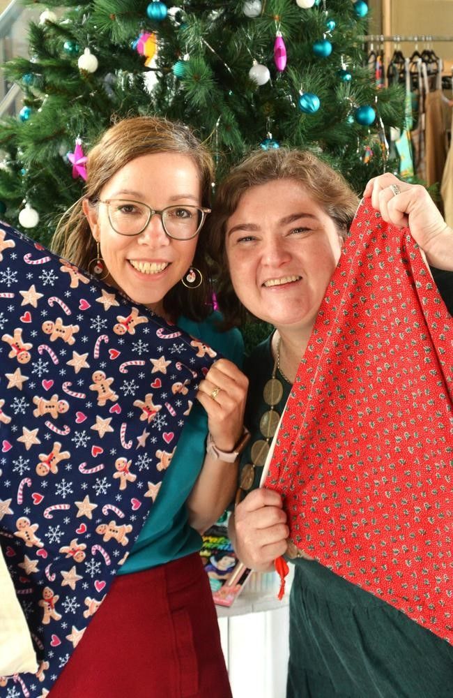 Two women are holding a piece of fabric in front of a christmas tree.