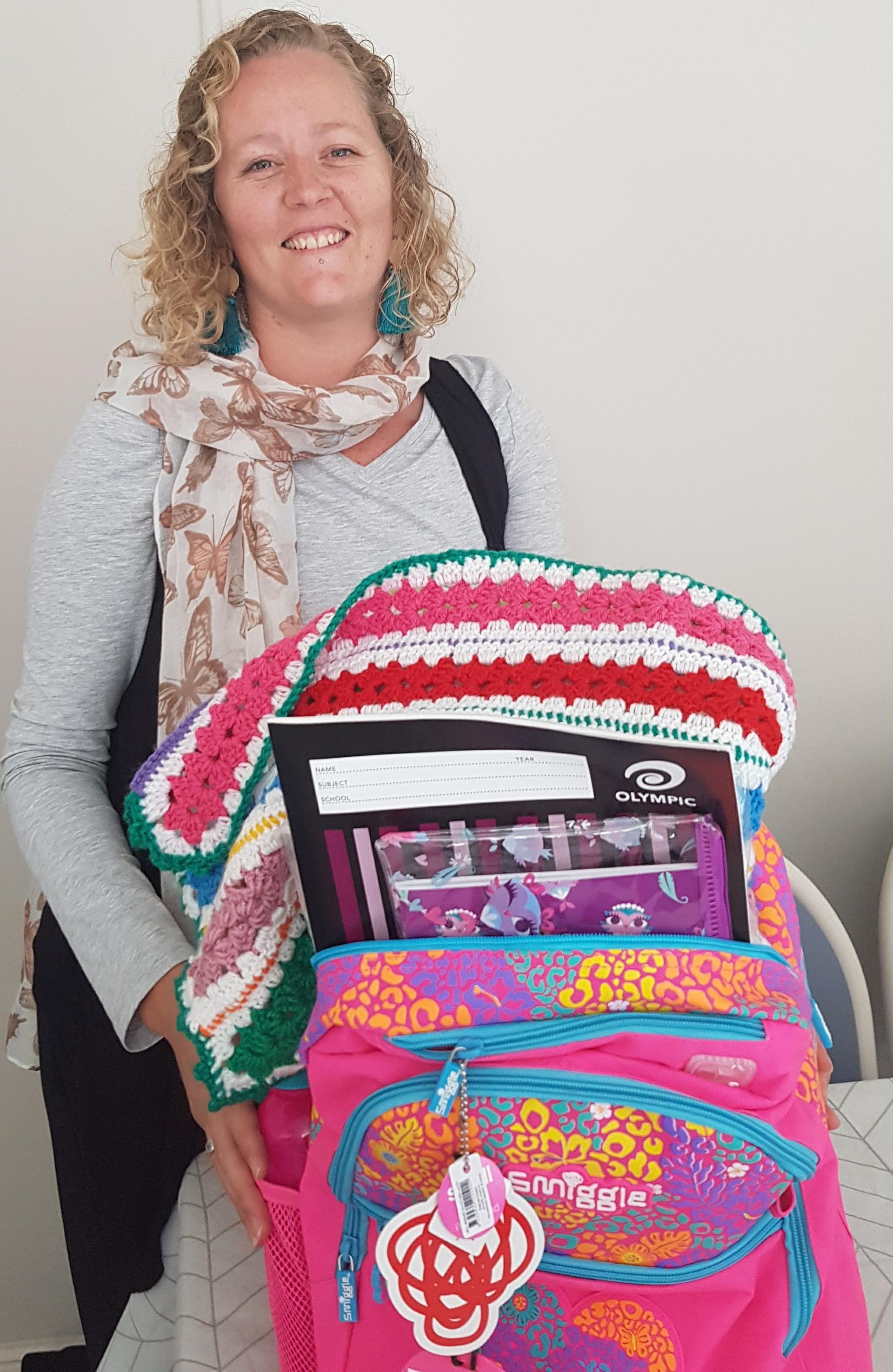 A woman is holding a pink backpack filled with school supplies.