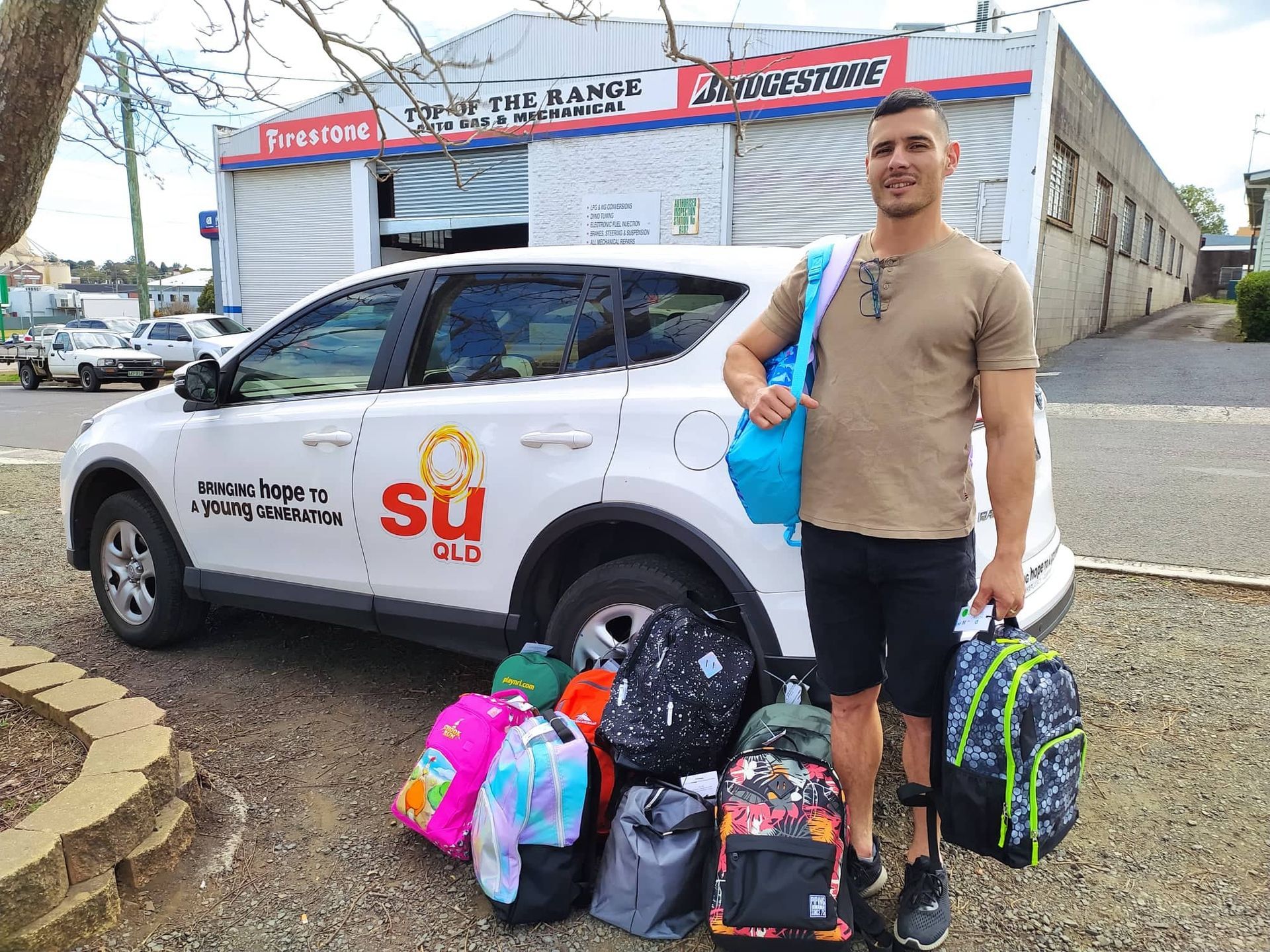 A man is standing in front of a car holding backpacks.