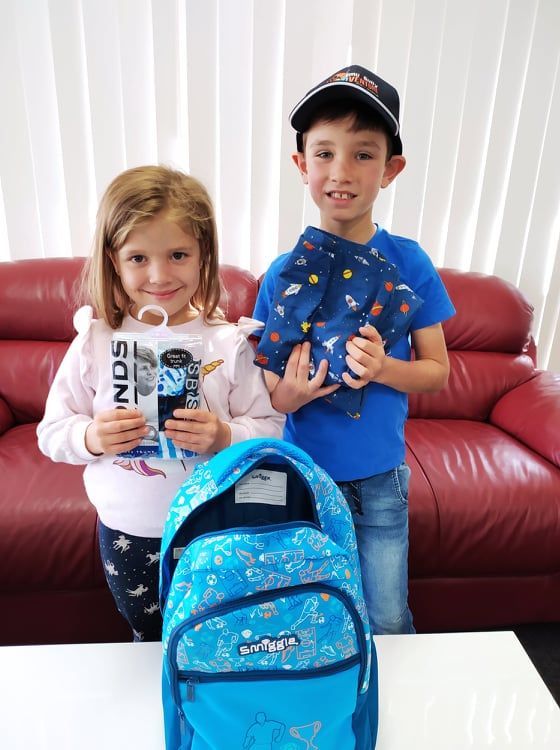 A boy and a girl are standing next to each other holding backpacks.