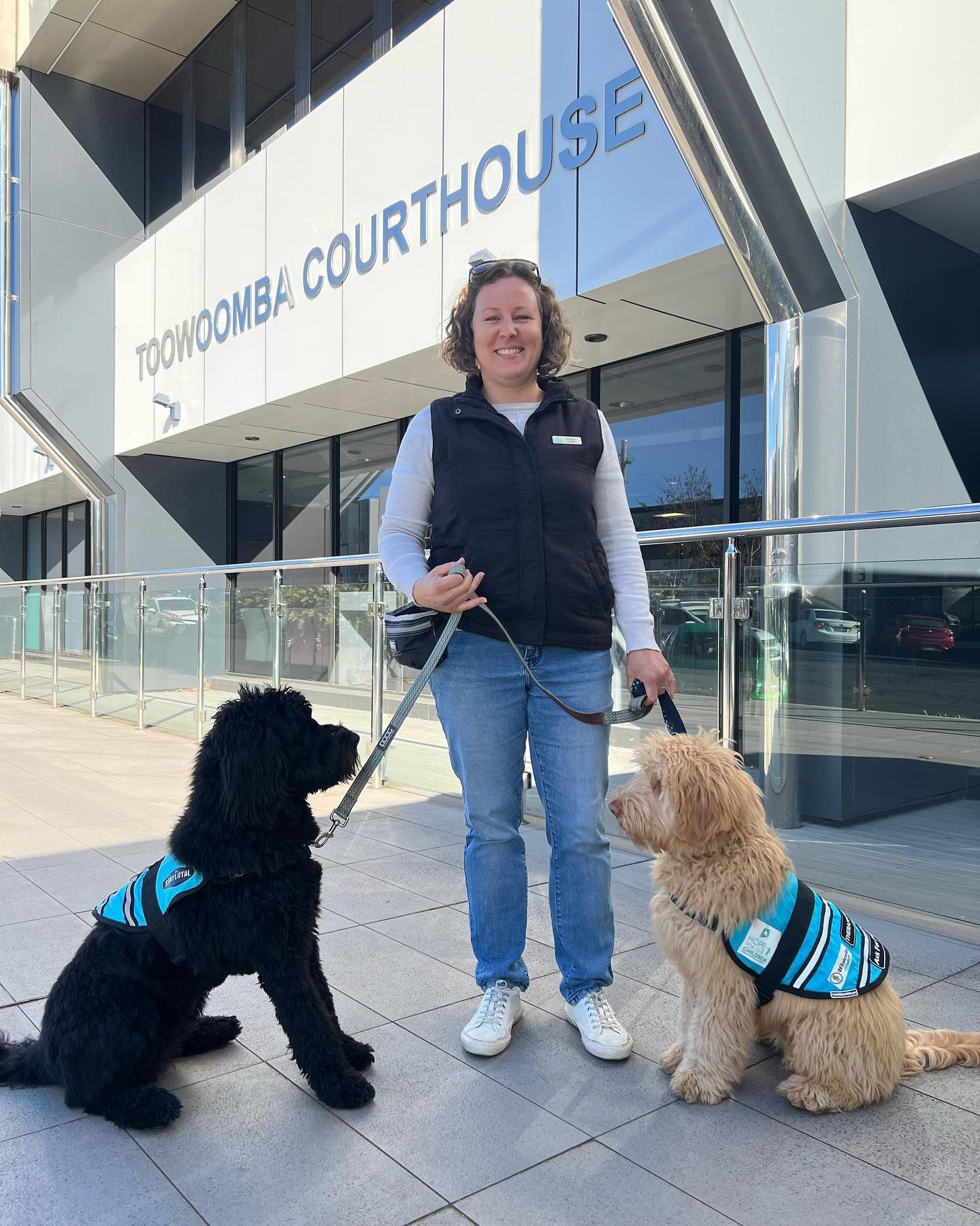 A woman is standing next to two service dogs in front of a building.