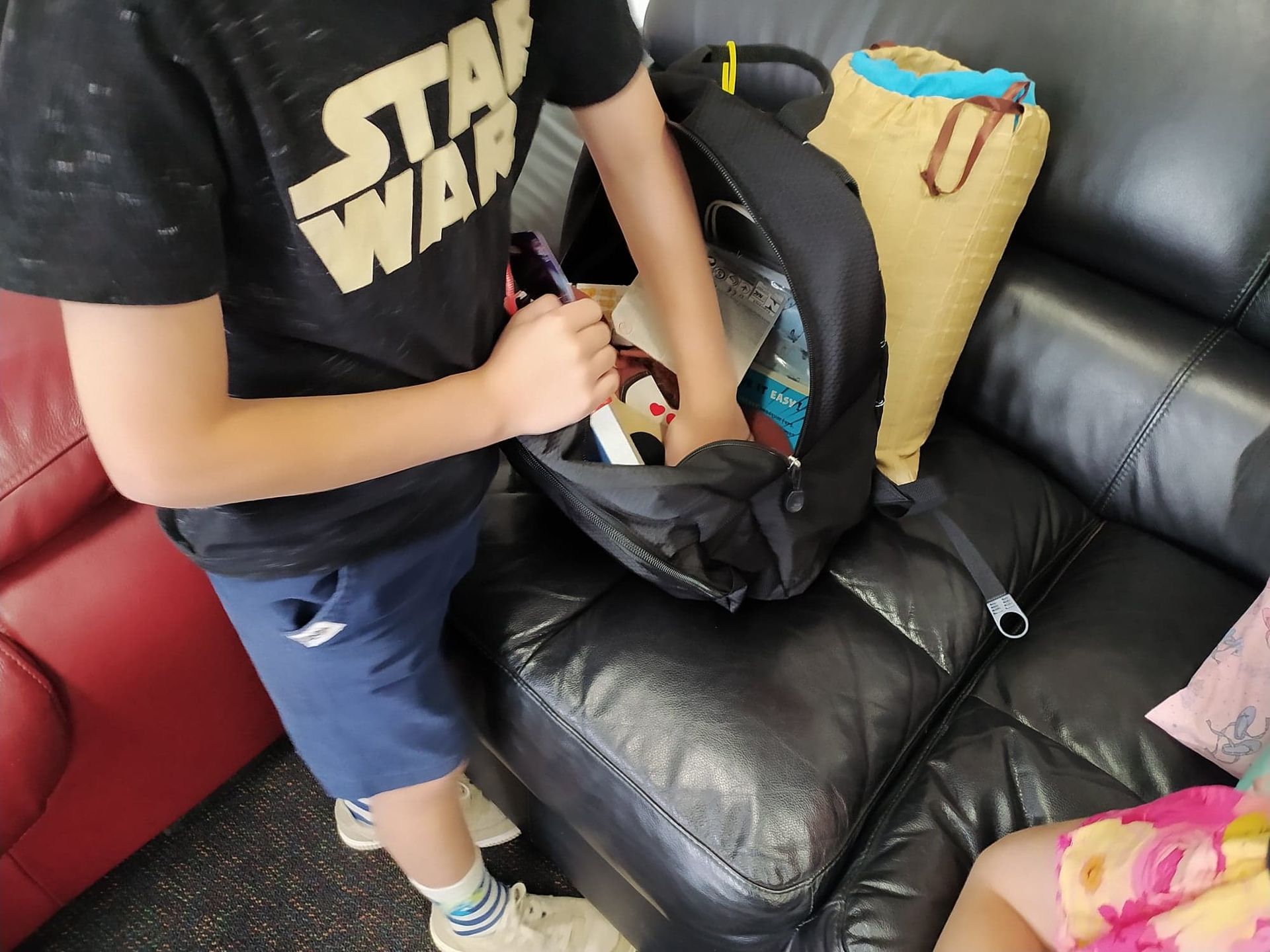 A boy wearing a star wars shirt is packing his backpack