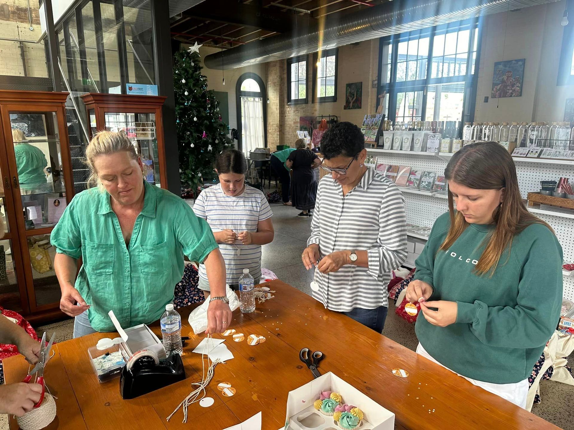 A group of people are sitting around a table making christmas decorations.
