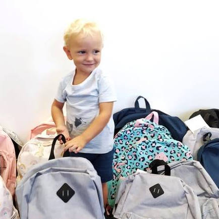 A little boy is standing in front of a pile of backpacks.