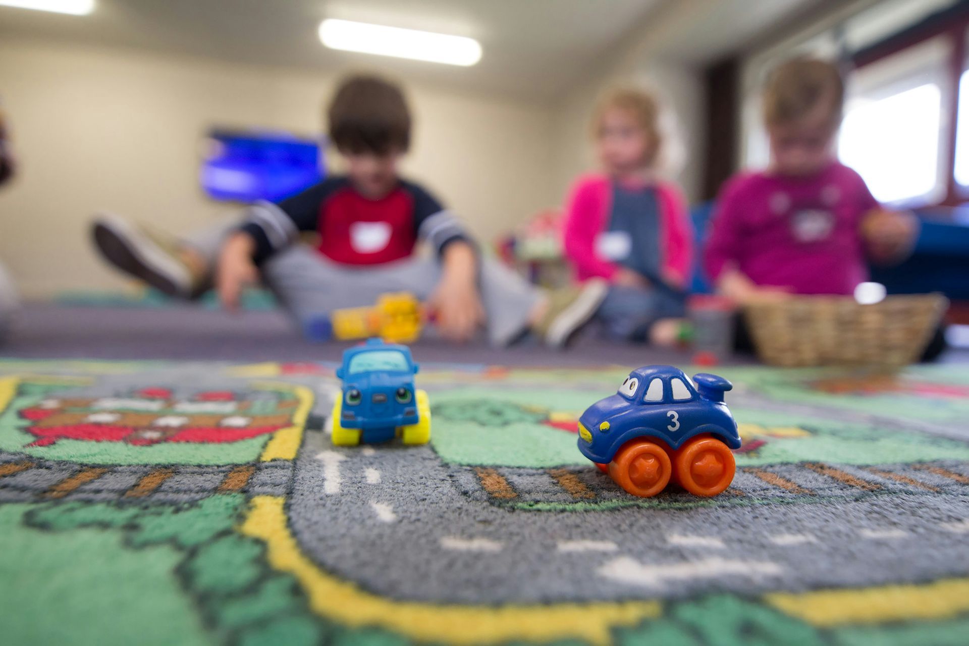 A group of children are playing with toy cars on a rug.